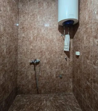 Manje kupatilo obloženo smeđim pločicama sa bojlerom i tušem. - image 10