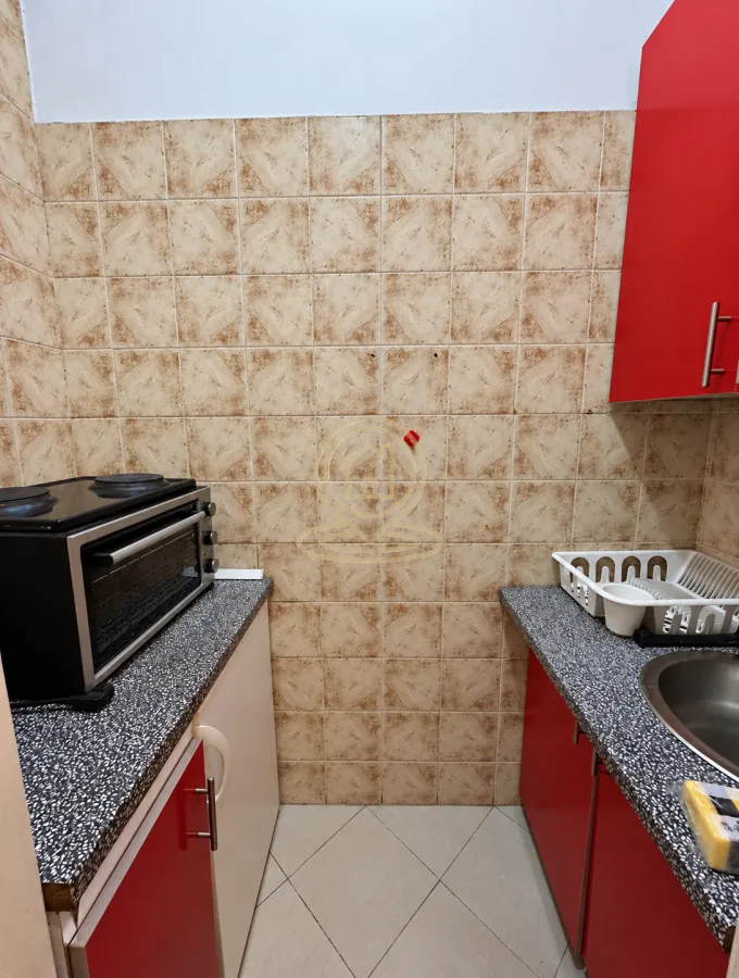 Manja kuhinja sa crvenim elementima i keramičkim pločicama na zidu.