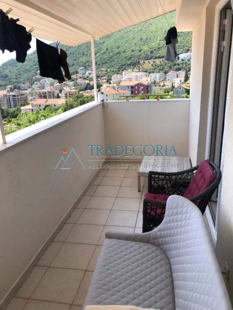 Natkriveni balkon sa garniturom za sjedenje i pogledom na naselje i brda.