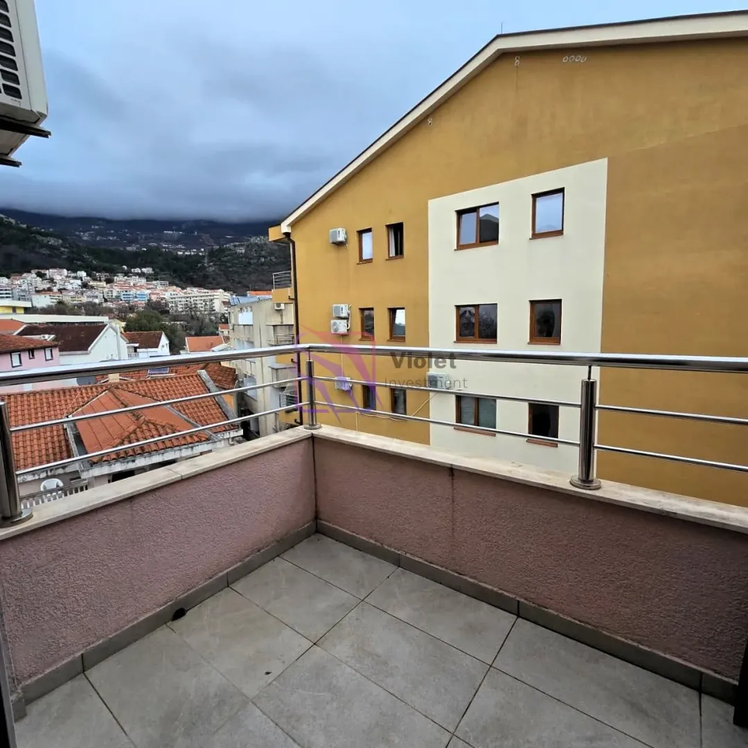 Manji popločani balkon sa metalnom ogradom i pogledom na naselje i okolne zgrade.
