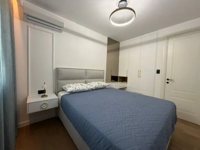 Moderna spavaća soba sa bračnim krevetom, bijelim plakarom i klima uređajem.