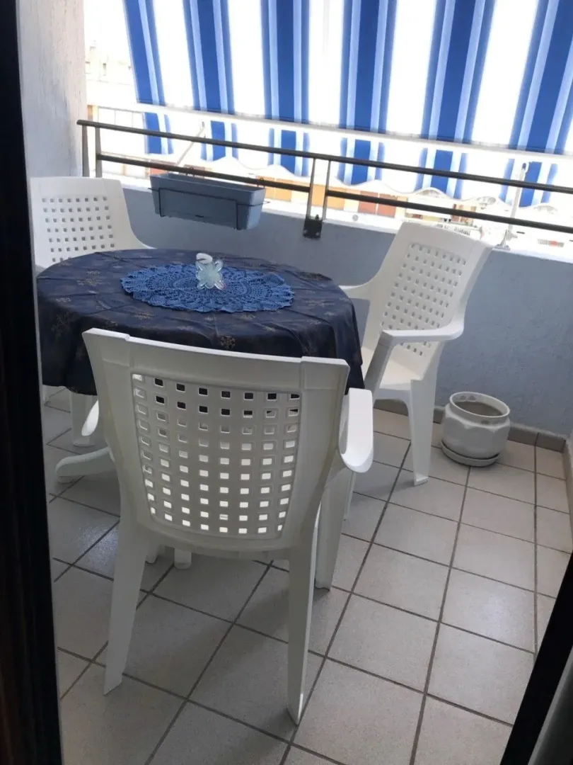 Balkon sa stolom i bijelim plastičnim stolicama pod tendom.