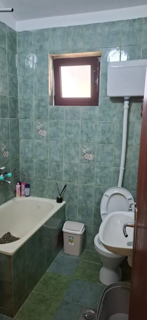Manje kupatilo obloženo zelenim pločicama sa kadom, toaletom i umivaonikom.