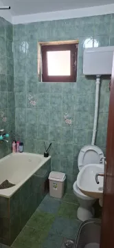 Manje kupatilo obloženo zelenim pločicama sa kadom, toaletom i umivaonikom. - image 9