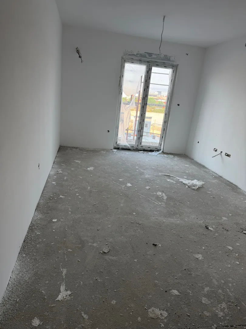 Prazna prostorija u izgradnji sa bijelim zidovima i balkonskim vratima.