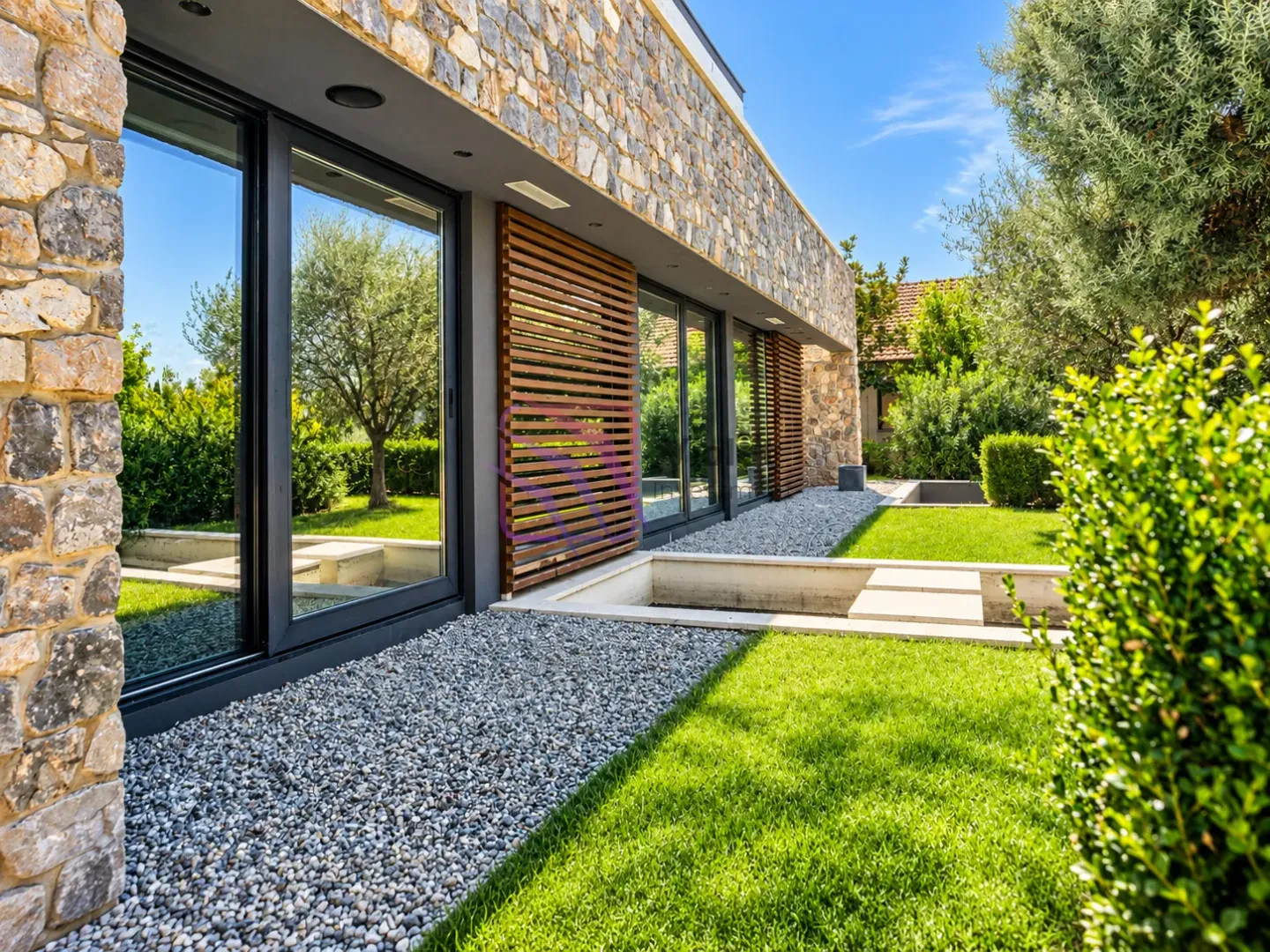 Exterior of a modern house with stone facade, large glass surfaces and landscaped yard.