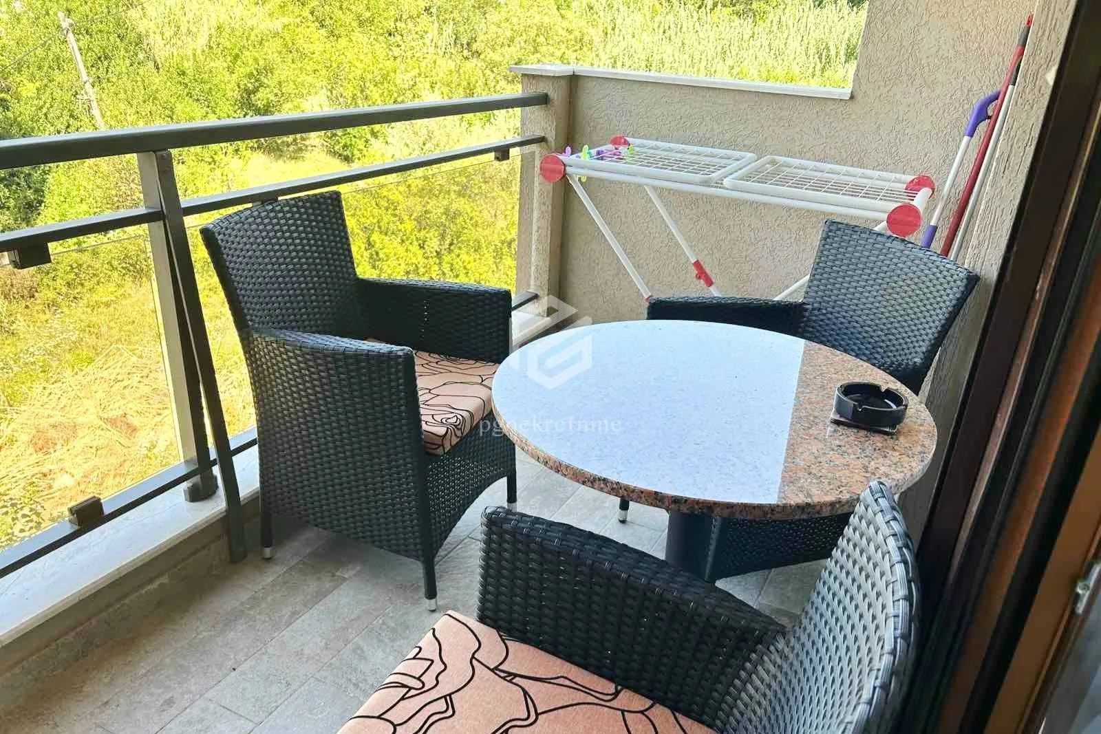 Namješten balkon sa stolom, stolicama i pogledom na zelenilo.