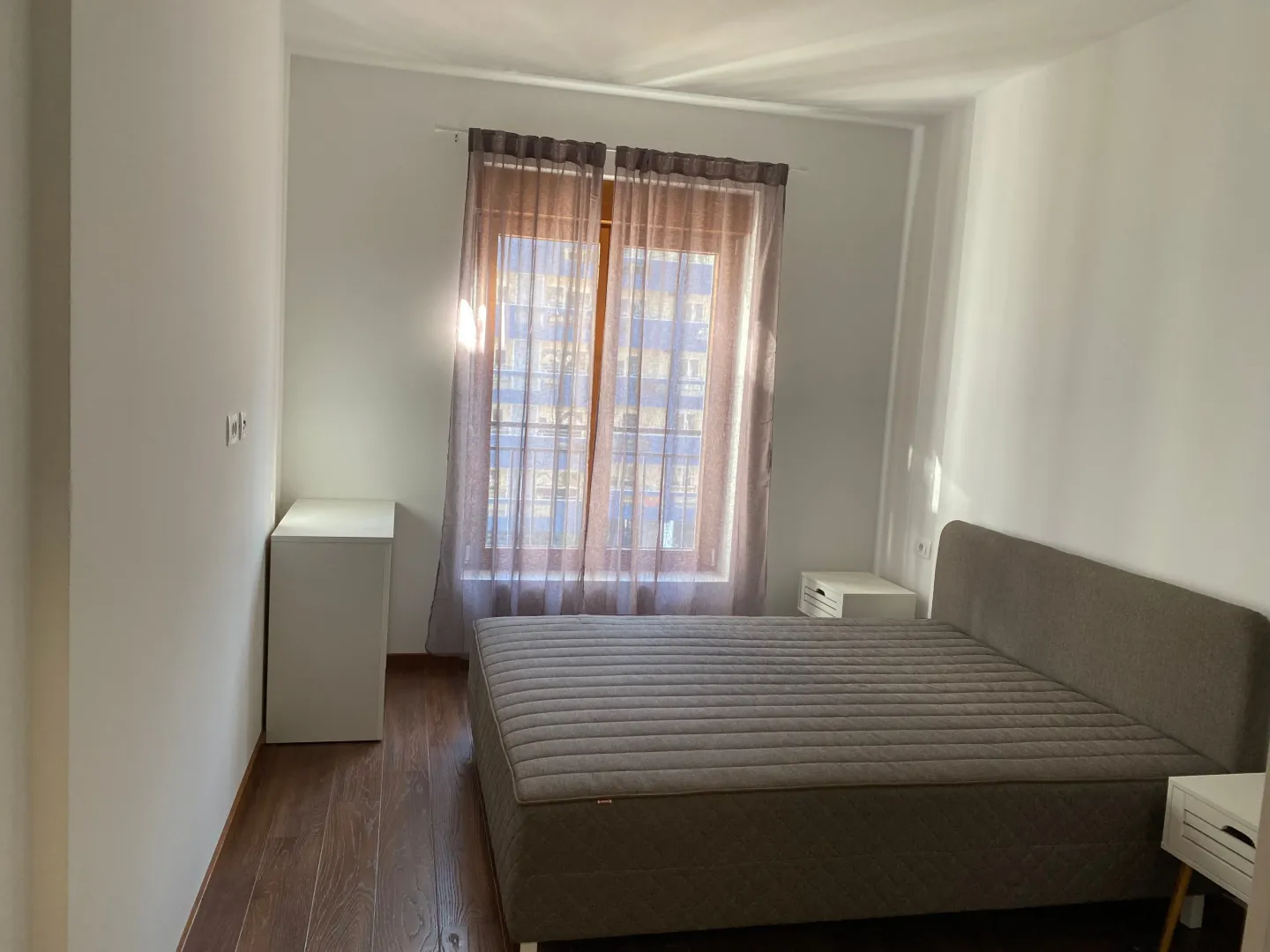 Bedroom with a double bed, white bedside tables, and a window with curtains.
