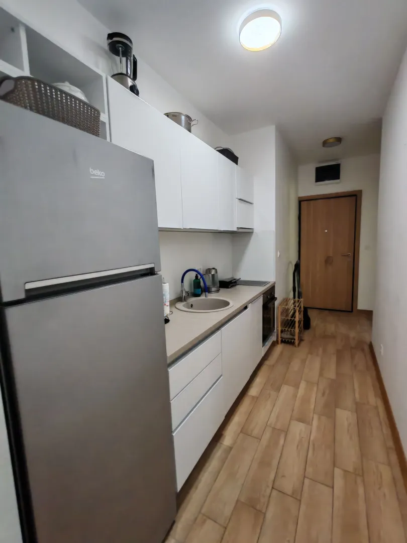 Small white kitchen with a refrigerator and wooden flooring.