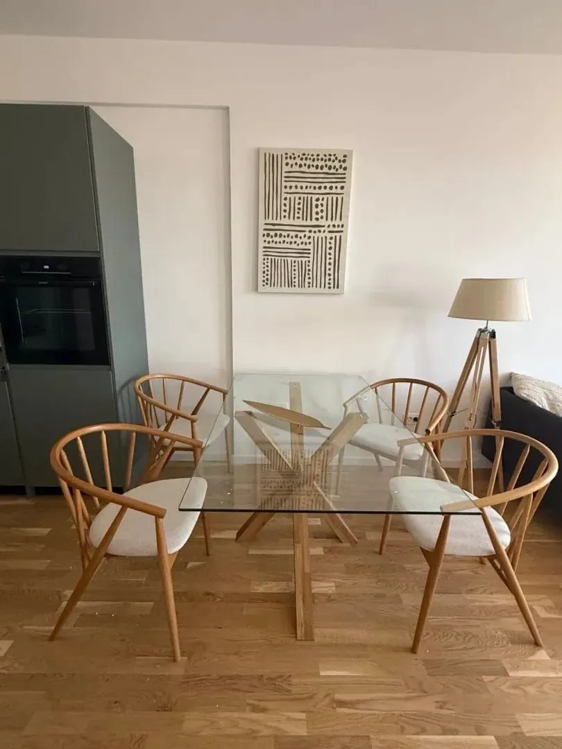 Dining area with a glass table and wooden chairs in a bright interior.
