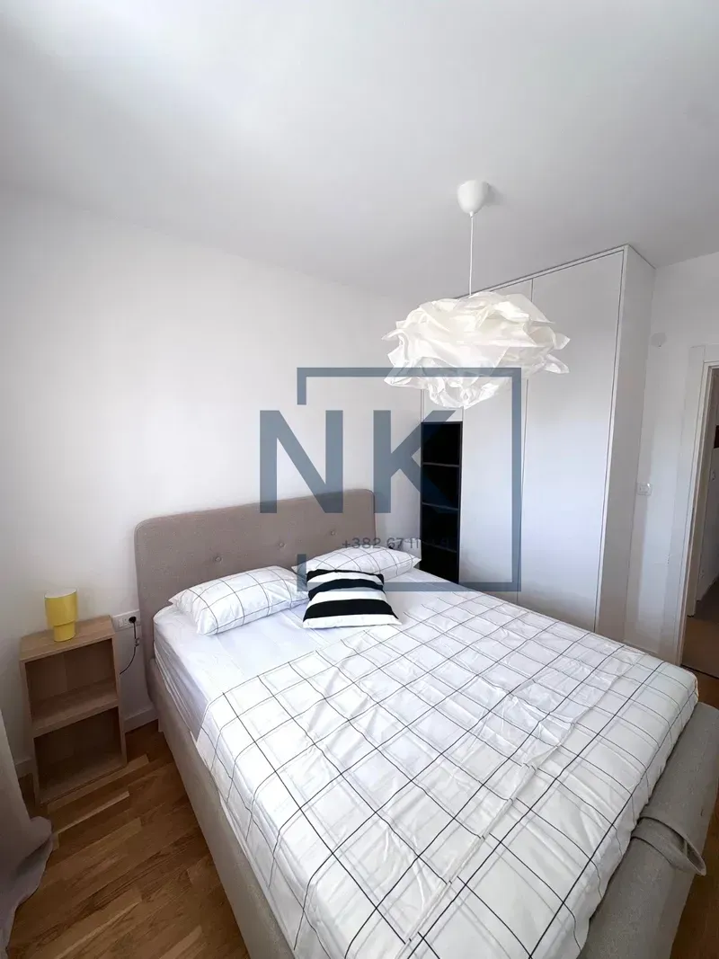 Namještena spavaća soba sa bračnim krevetom, garderoberom i lusterom.