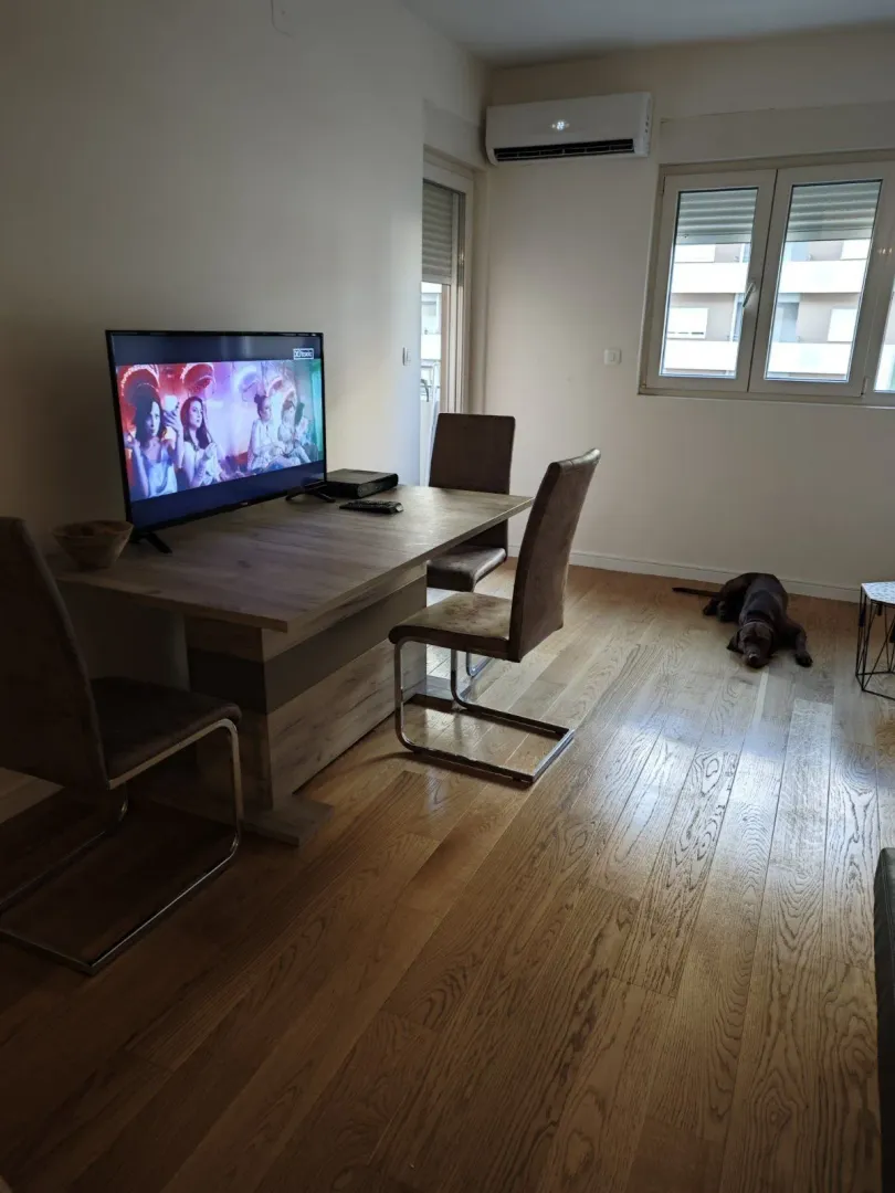 Dnevna soba sa drvenim stolom, televizorom i klima uređajem.