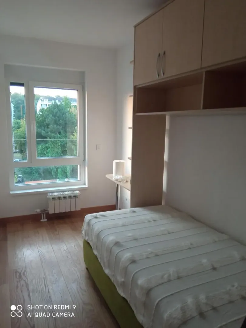 Small bedroom with a bed, wooden flooring, and a window overlooking greenery.