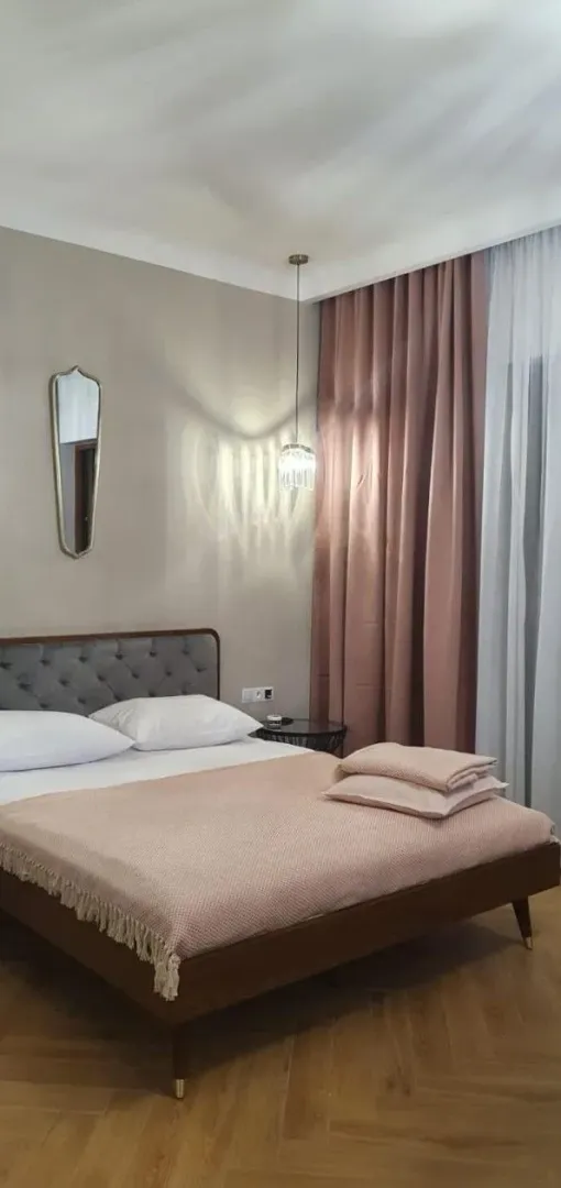 Uređena spavaća soba sa bračnim krevetom, zavesama i detaljima.