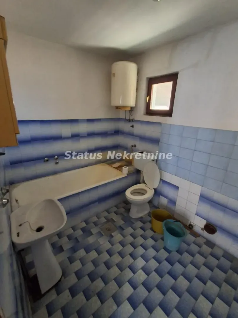 Starije kupatilo sa kadom, umivaonikom, WC šoljom i bojlerom.