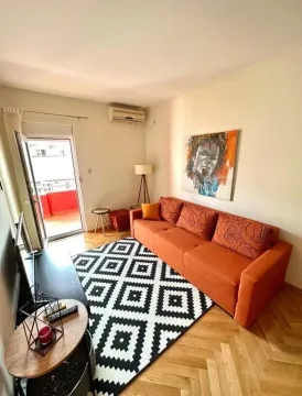 Svijetla dnevna soba sa narandžastom sofom, crno-bijelim tepihom i izlazom na balkon. - image 15