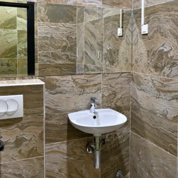 Bathroom lined with brown marble tiles featuring a white sink and a mirror. - image 5