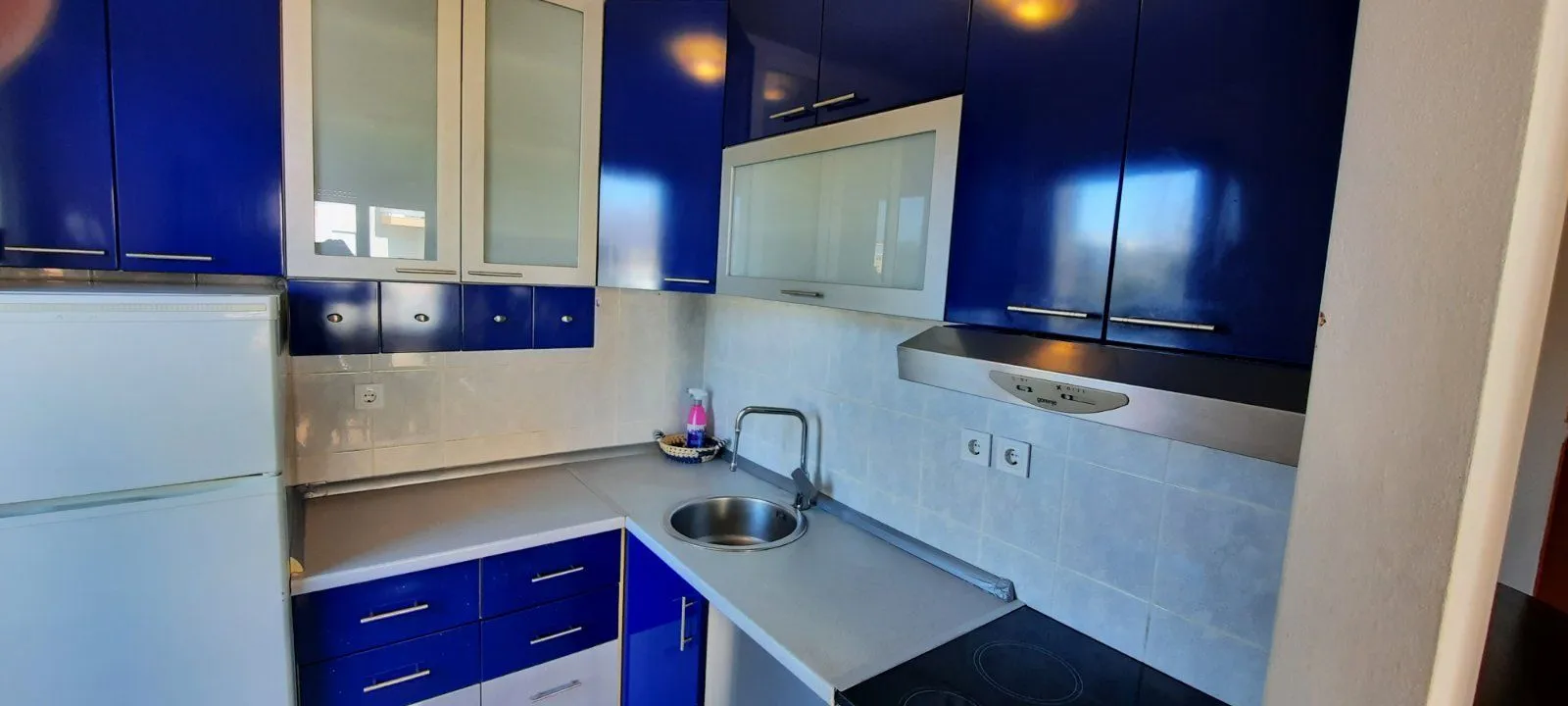 Small kitchen with blue and white cabinets, a sink, and a built-in cooktop.