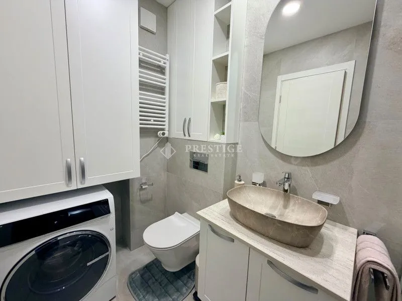 Modernly equipped bathroom with a washbasin, toilet, built-in cabinets, and washing machine.