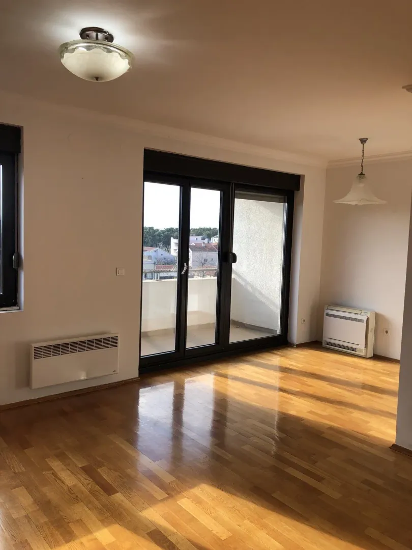 Bright empty room with wooden flooring and access to a balcony.