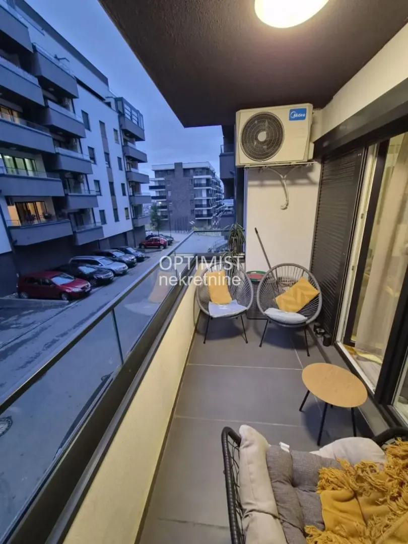 Namešten balkon sa garniturom za sedenje i pogledom na naselje i parking.