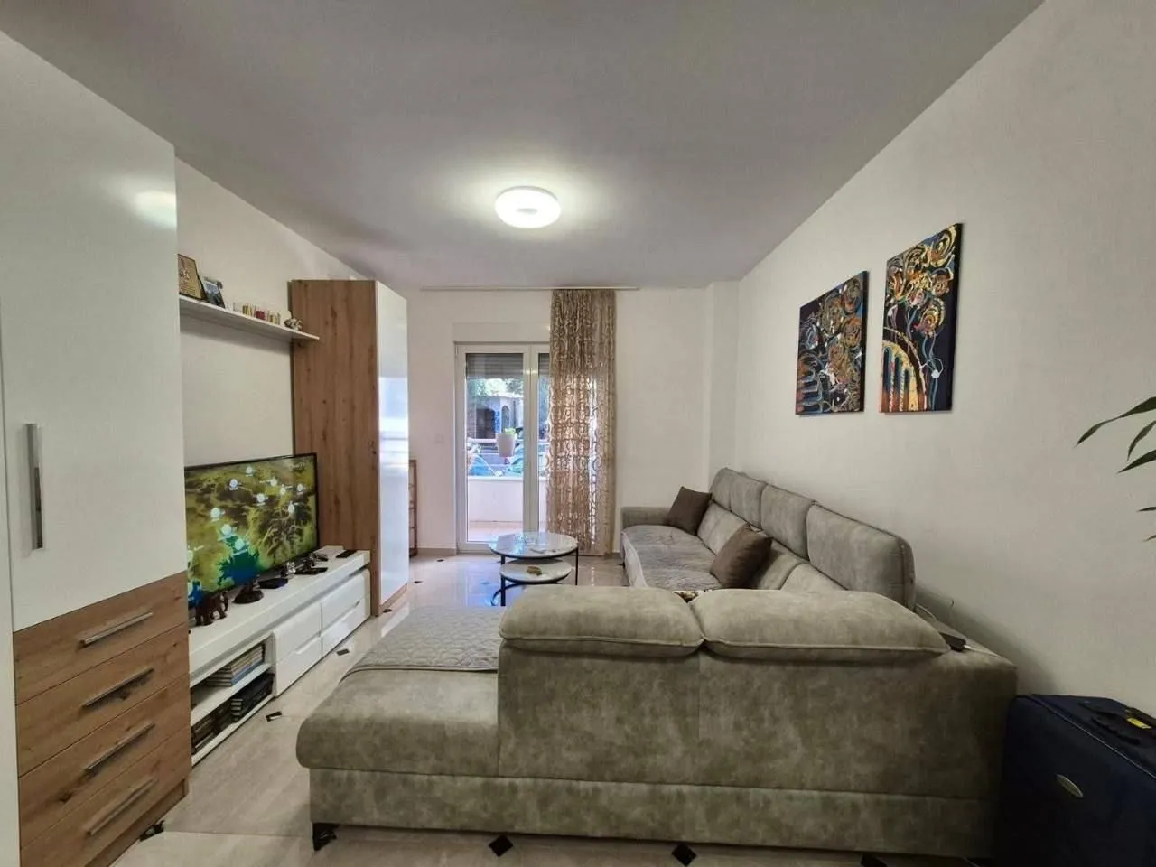 Comfortable living room with a sectional sofa, TV unit, and paintings on the wall.