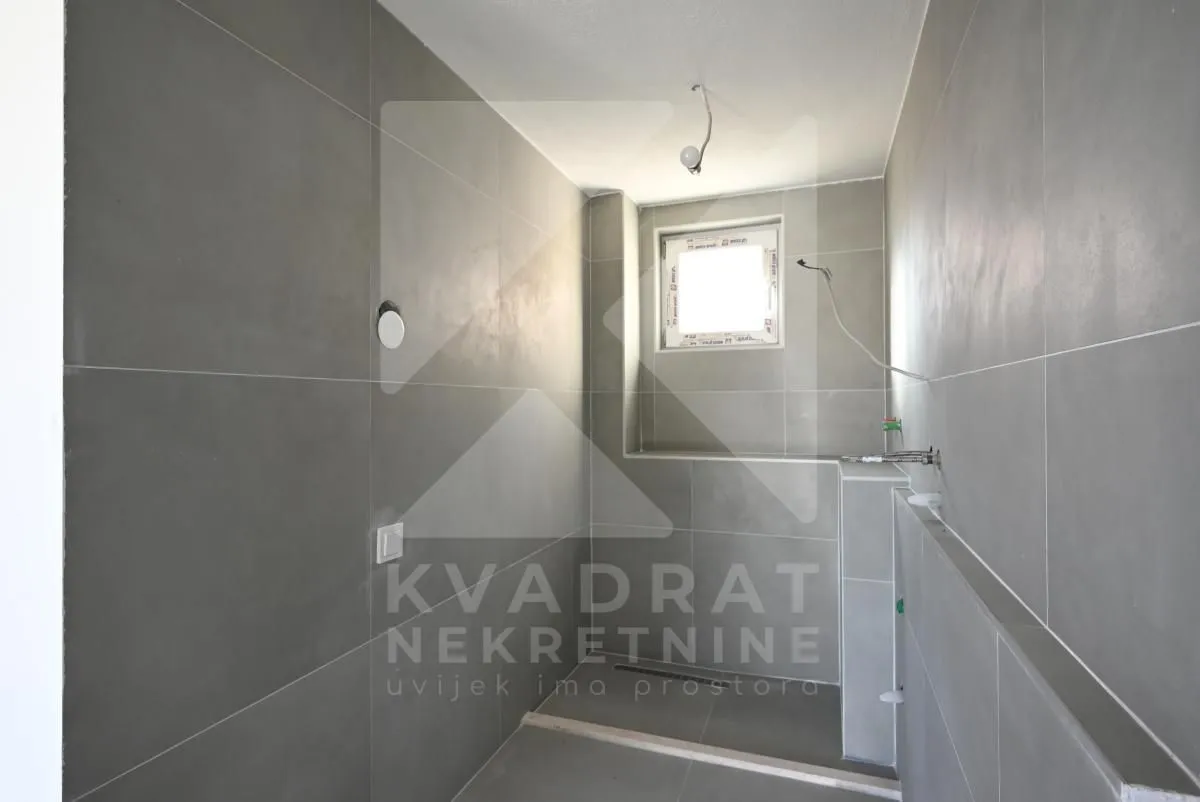 Bathroom under construction tiled in gray with a small window.