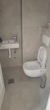 Small bathroom lined with grey tiles featuring a toilet and a washbasin. - image 2