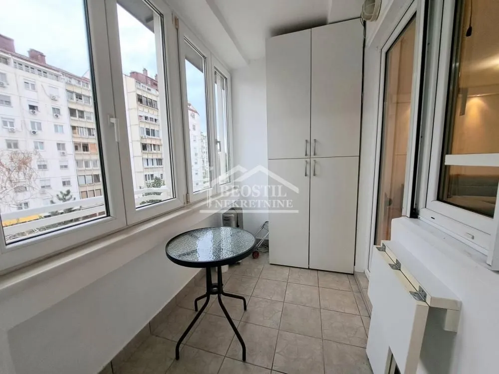 Zastakljeni balkon sa malim stolom i ugradnim ormarom.