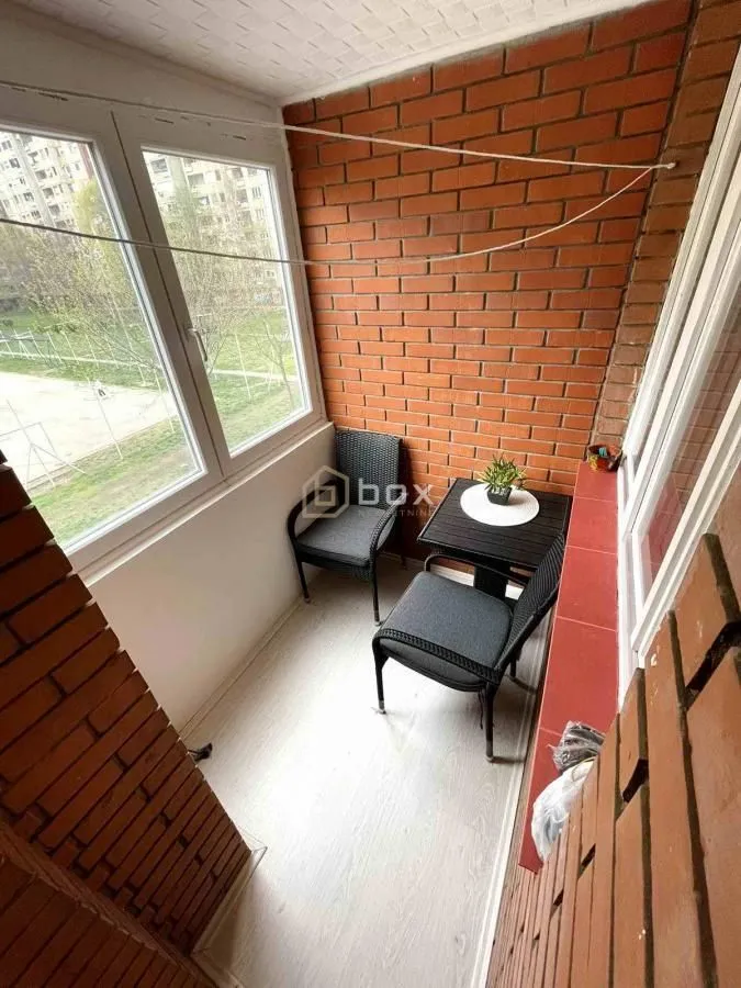 Zastakljeni balkon sa malim stolom i stolicama.