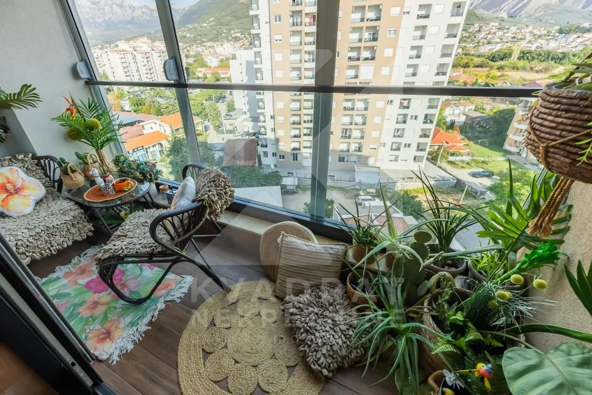 Uređen zatvoreni balkon sa garniturom za sjedenje i ukrasnim biljkama.