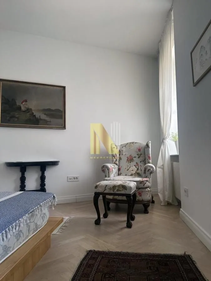 Spavaća soba sa krevetom, foteljom i umetničkim slikama na zidu.