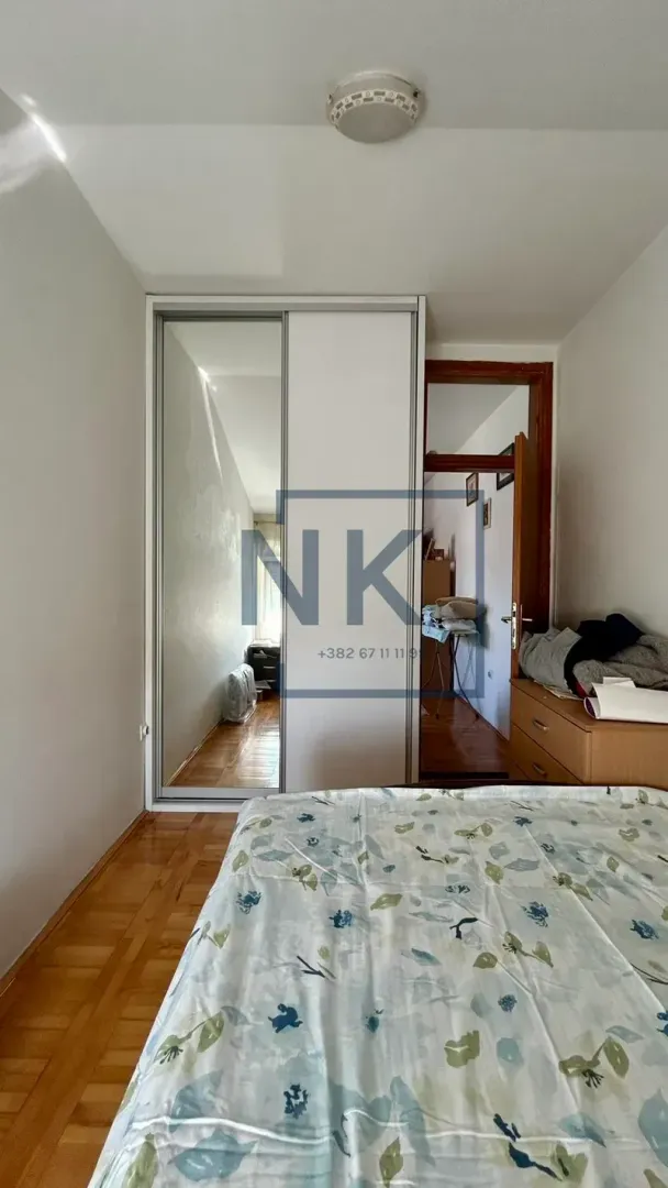 Namještena spavaća soba sa bračnim krevetom, ugradnim plakarom i drvenim podom.