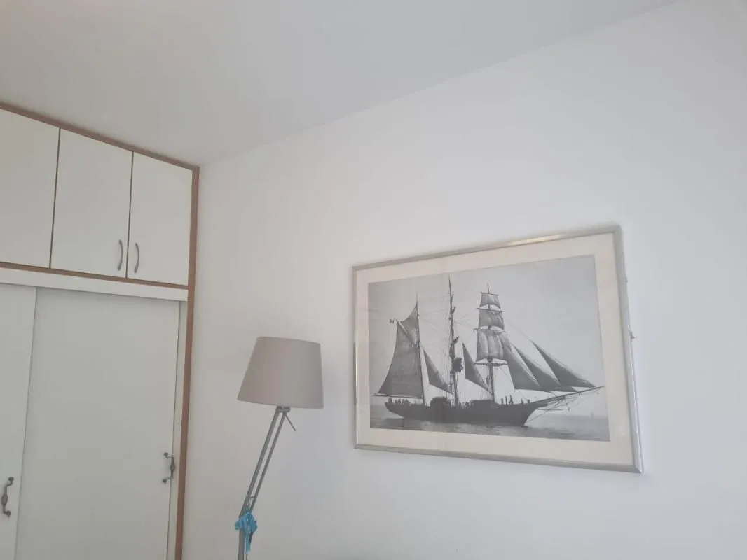 Detalj bijelog zida sa ugradnim plakarom, lampom i uramljenom slikom jedrenjaka.