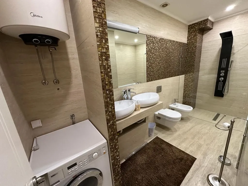 Modern bathroom with double sinks, walk-in shower, fixtures, and washing machine.