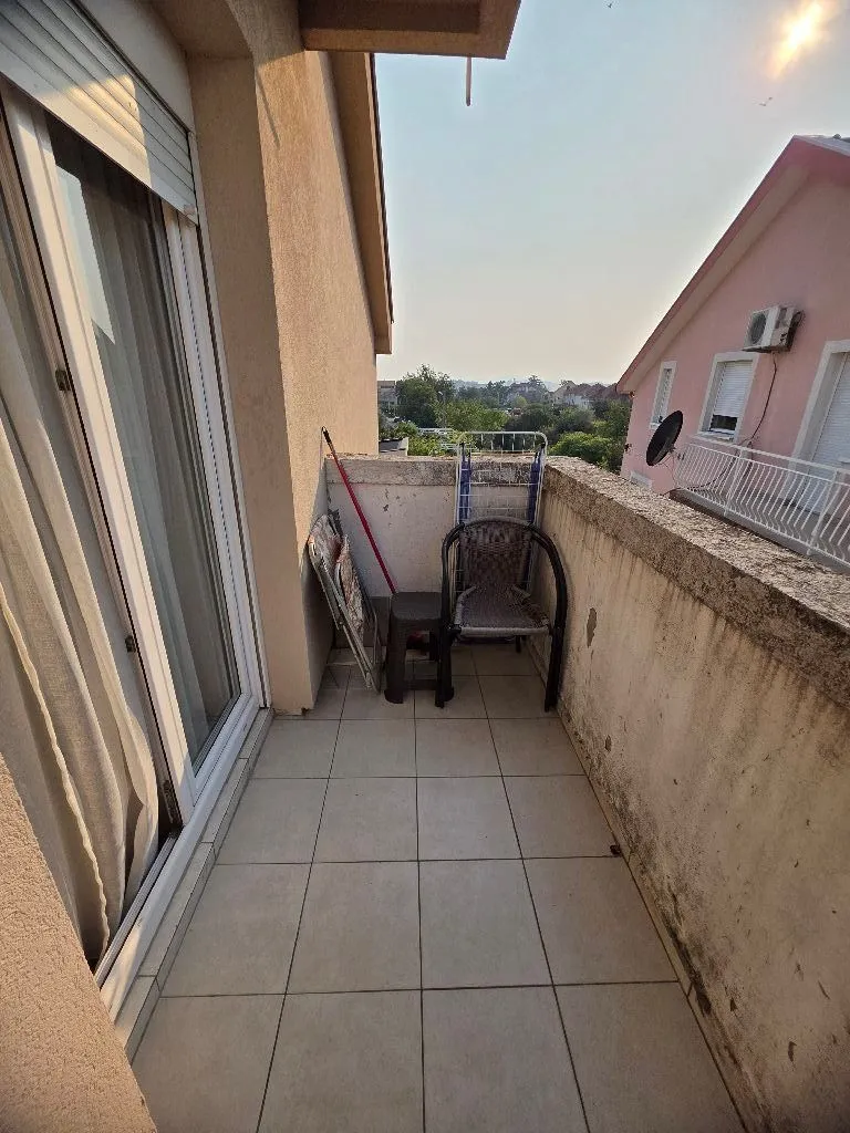 Manji popločani balkon sa stolicama i pogledom na okolne kuće.