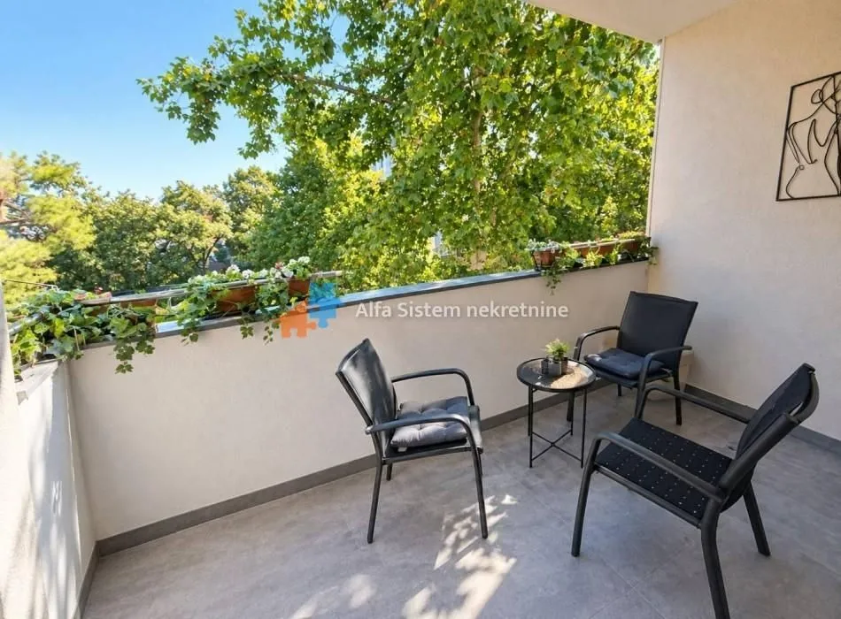 Namešten balkon sa garniturom za sedenje i pogledom na zelenilo.