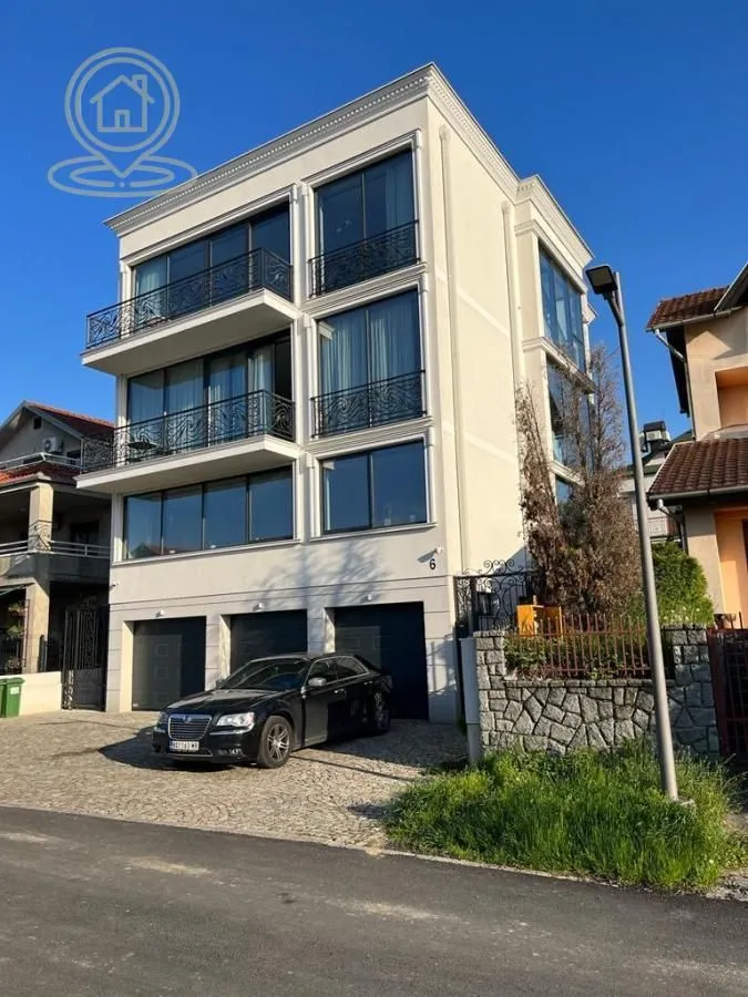 Pogled na spoljašnjost moderne stambene zgrade sa balkonima i garažama u prizemlju.
