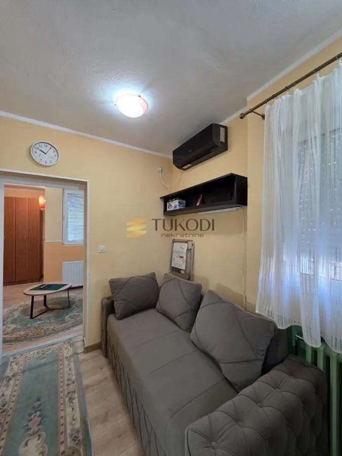 Small living room with a grey sofa, air conditioning unit, and a view of the adjacent room.