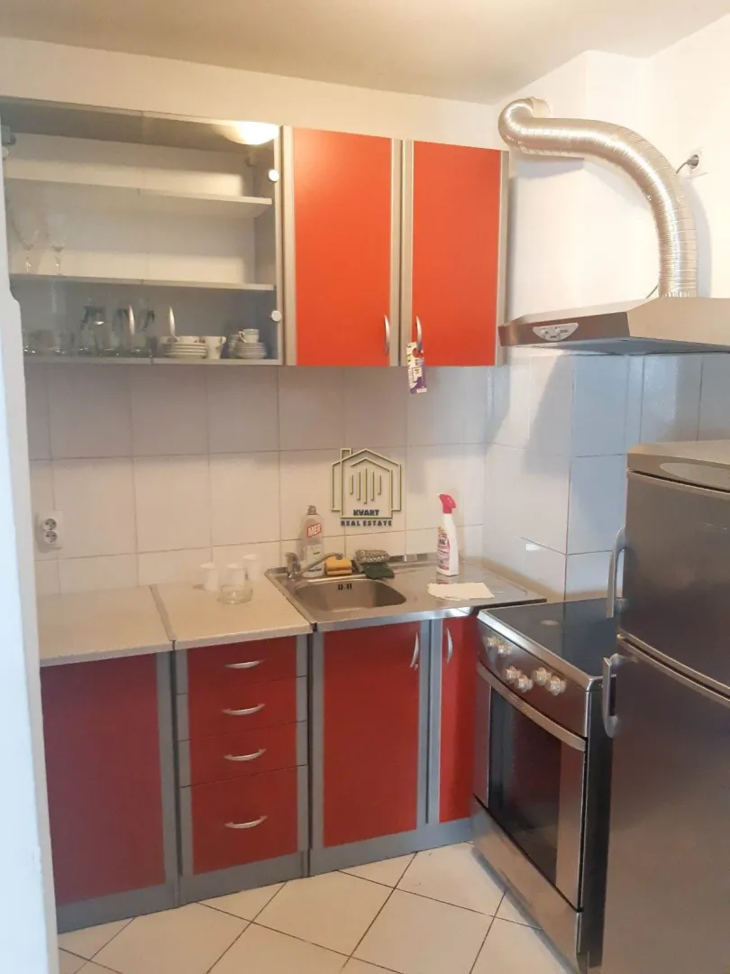Manja kuhinja sa crvenim elementima i šporetom.