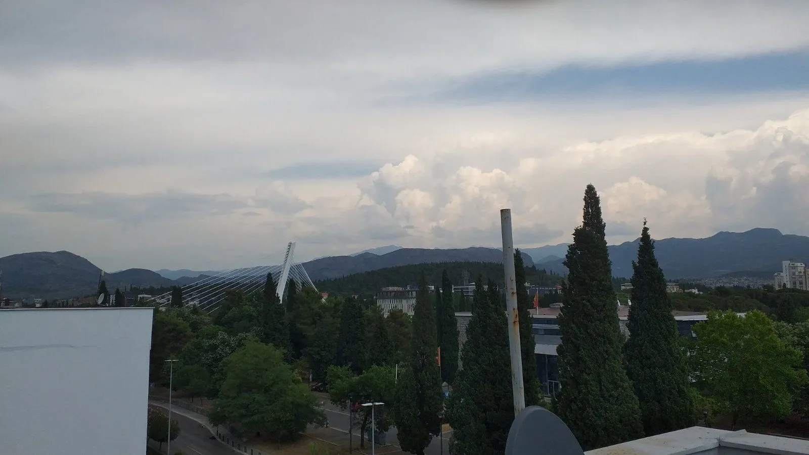 Elevated view of the city, bridge, and hills in the distance under a cloudy sky.
