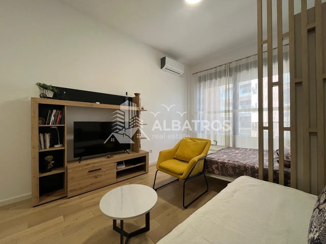 Living room with a TV unit, yellow armchair, and a bed.