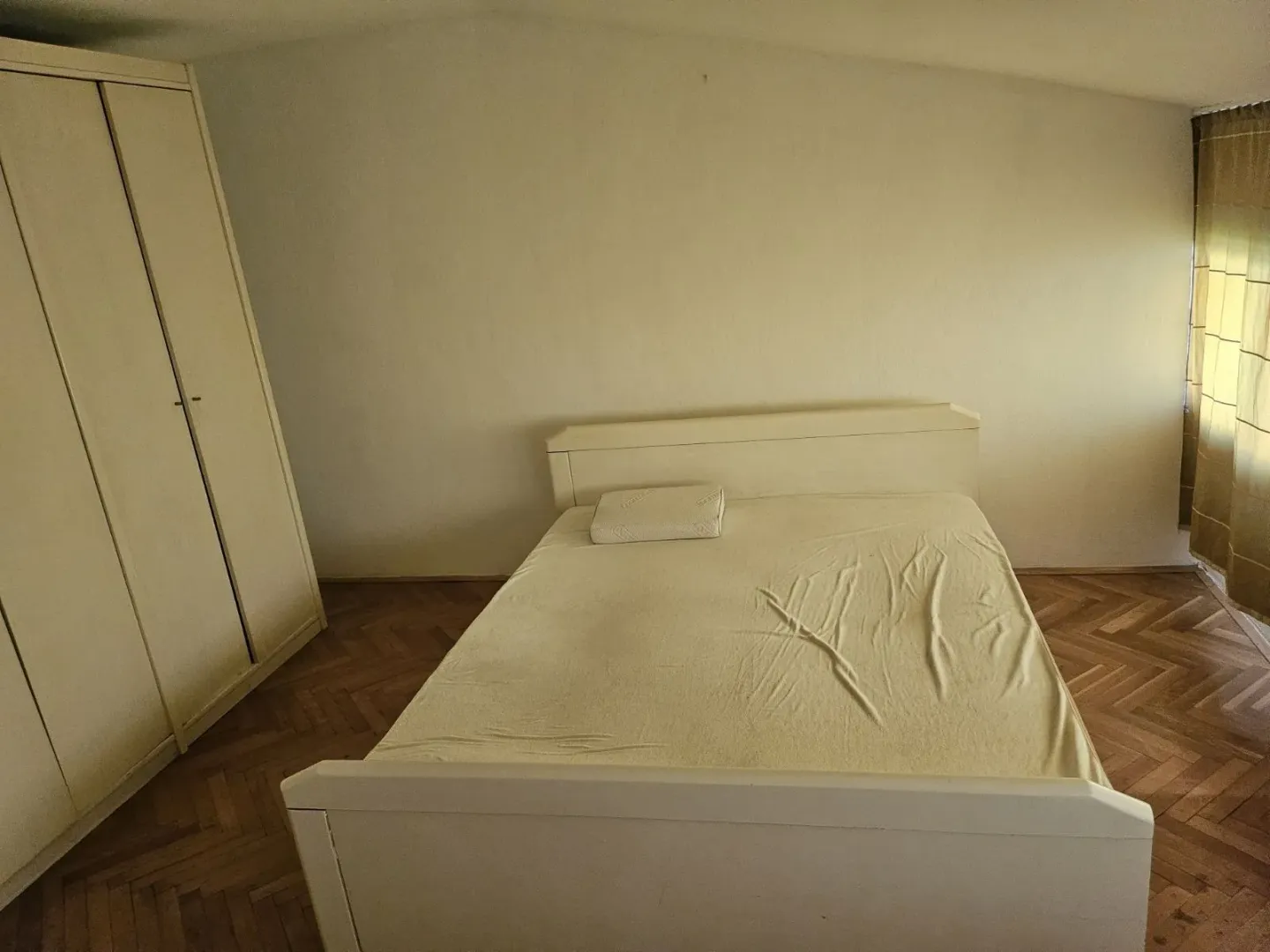 Jednostavno namještena spavaća soba sa bračnim krevetom i velikim ormarom.