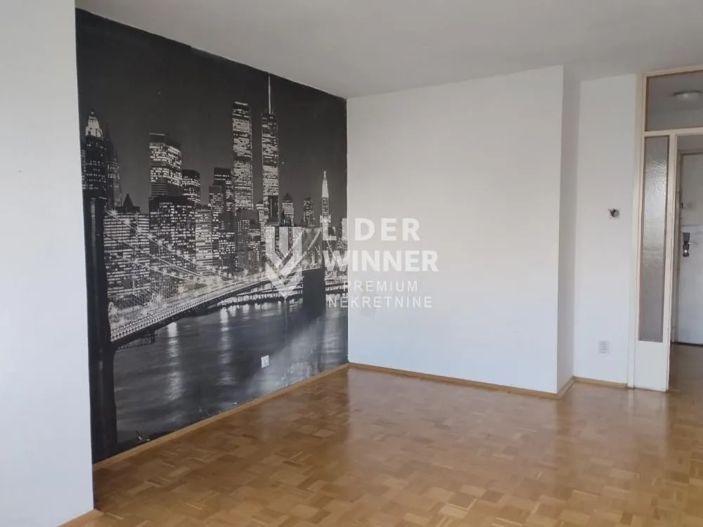 An empty room with a city-themed wallpaper on the wall and parquet flooring.