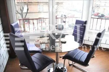 Dining table with chairs placed next to large windows with a street view.