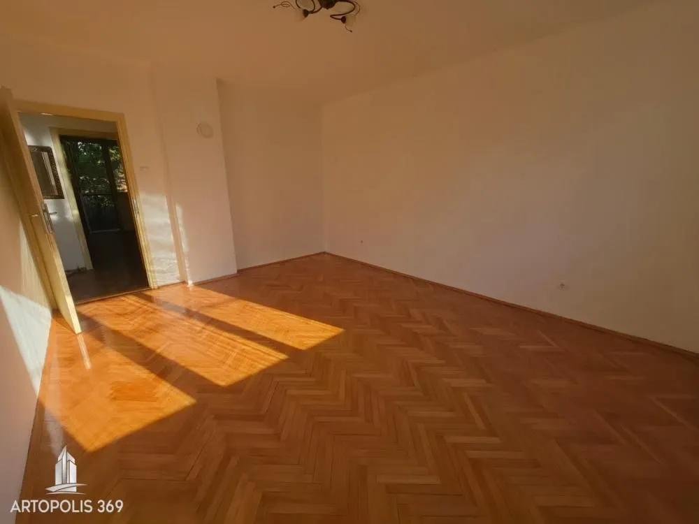 Prazna soba sa parketom i otvorenim vratima.