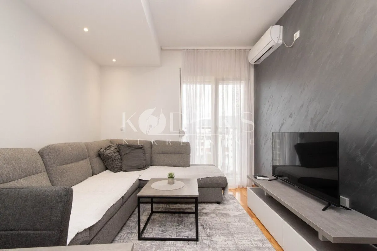 Living room with a sectional sofa, television, and air conditioning unit.