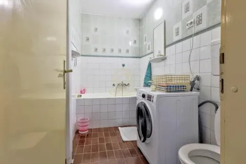 Bathroom with a bathtub, washing machine, and toilet. - image 6