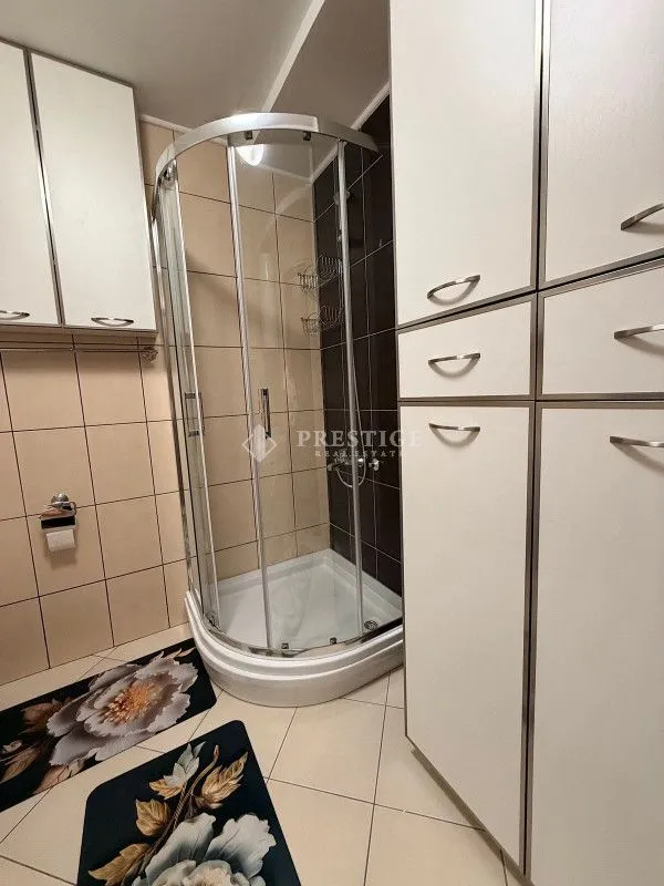 Manje kupatilo sa tuš kabinom i bijelim ormarićima.