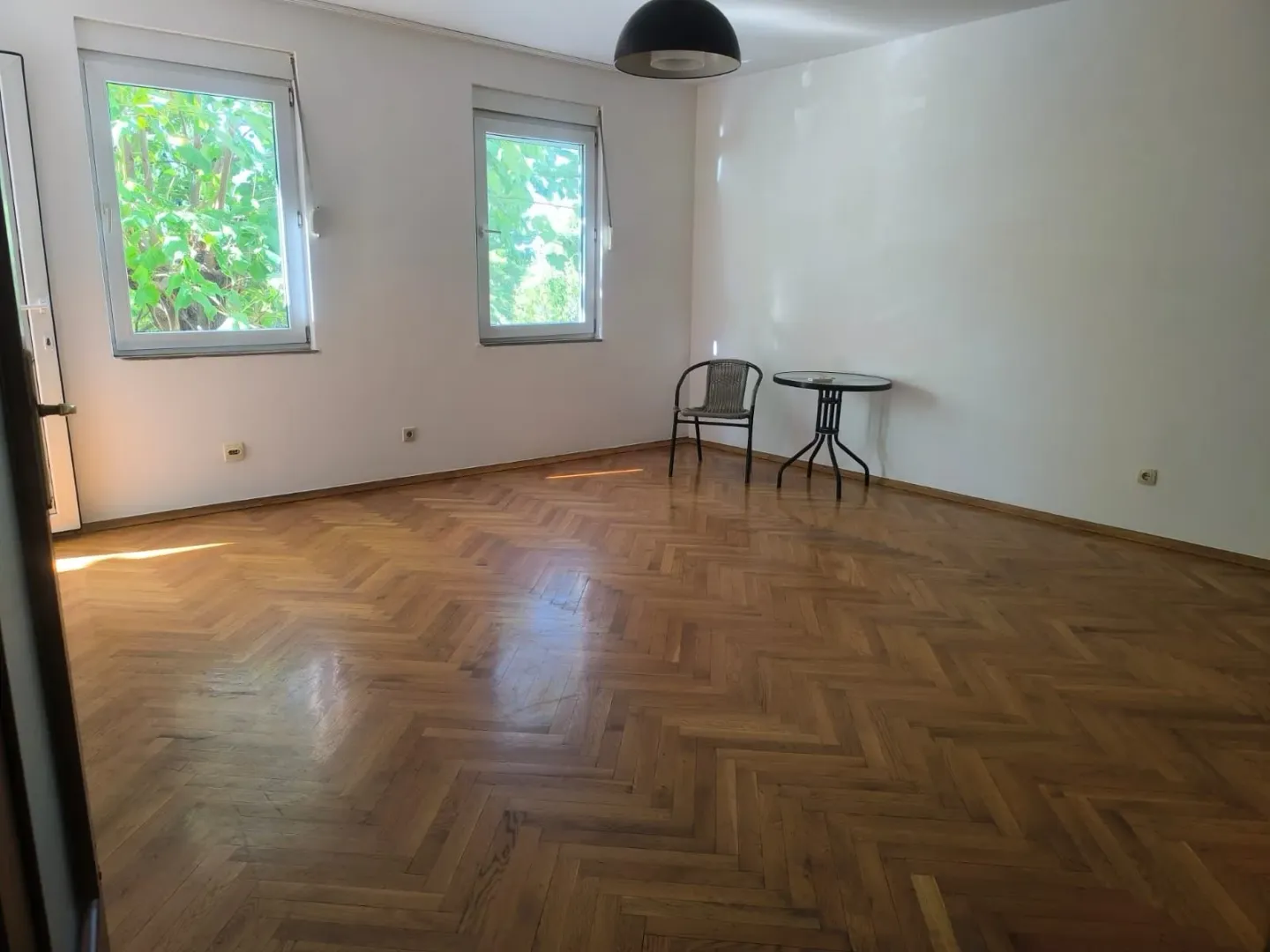 Prazna soba sa parketom i dva prozora.